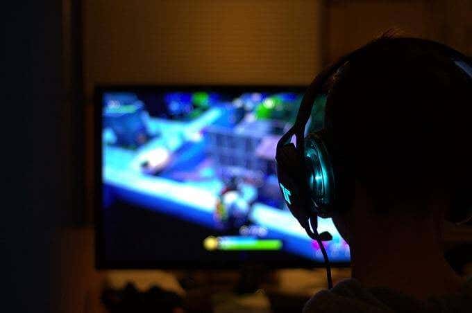 A person wearing headphones plays a video game on a computer monitor in a dark room