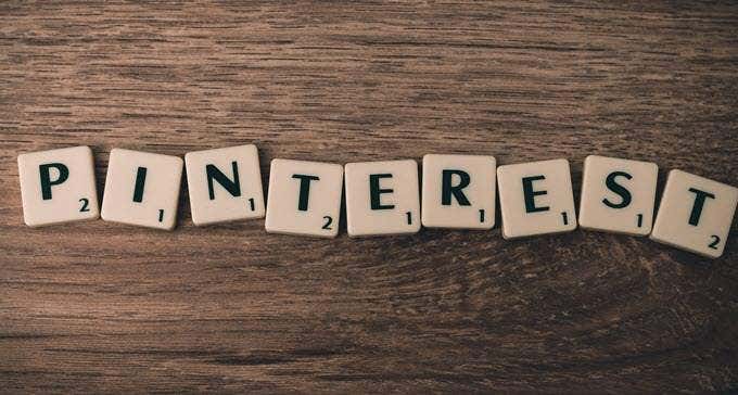 Square tiles spelling "PINTEREST" are arranged on a dark brown wooden surface