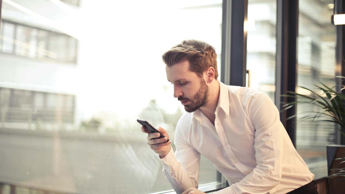 A man, wearing a white shirt, is looking at a smartphone