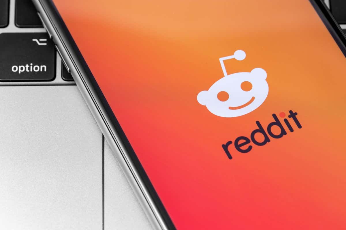 A smartphone displays the Reddit logo and name on an orange gradient background, resting on a laptop keyboard
