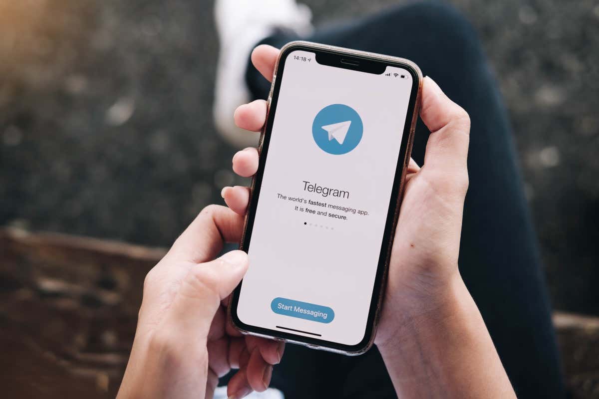 A smartphone displays the Telegram app's start-up screen; a person holds it, possibly about to begin messaging; the setting appears to be outdoors